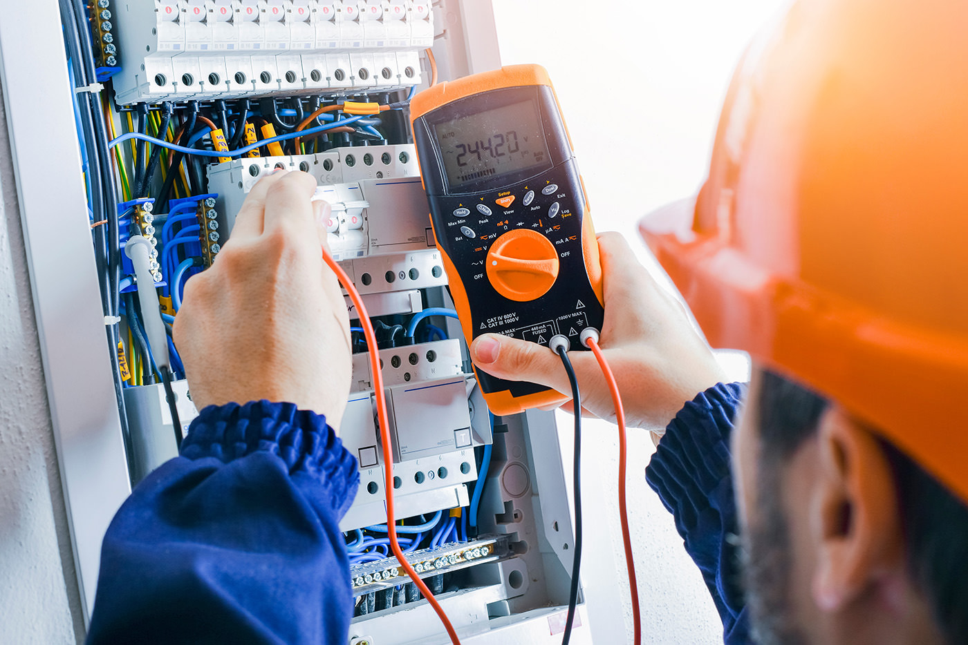 A man using a digital multimeter to measure electrical current in a circuit during an electrical installation.