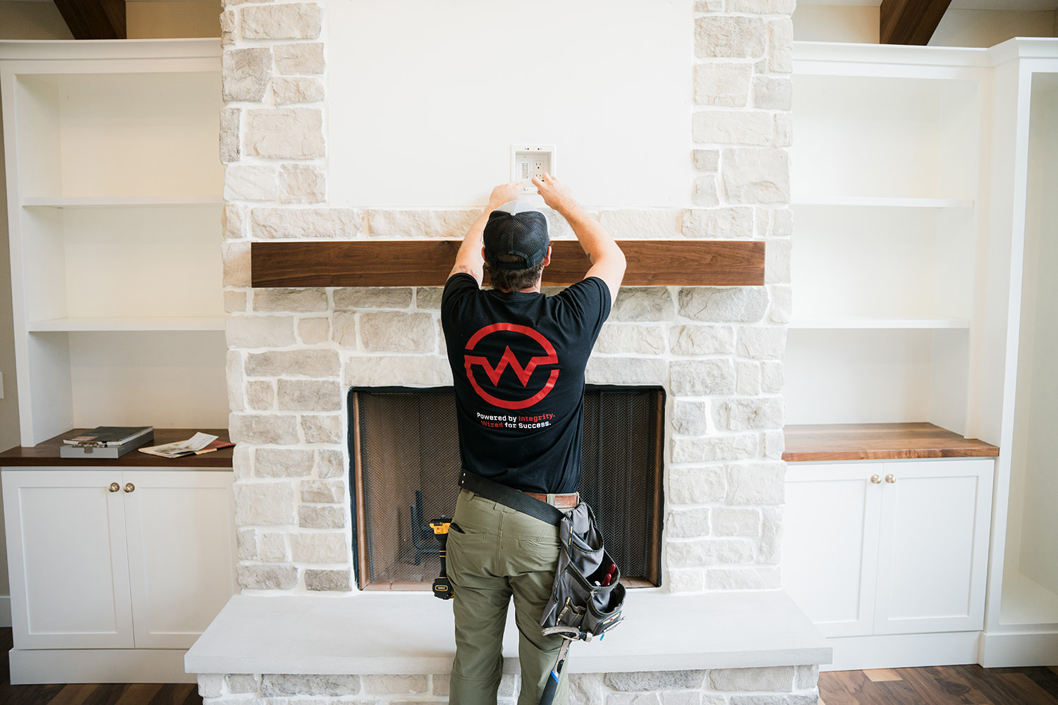 Professional Electrician installing an Electrical wall outlet above a mantle, representing home electrical safety and proper outlet installation.